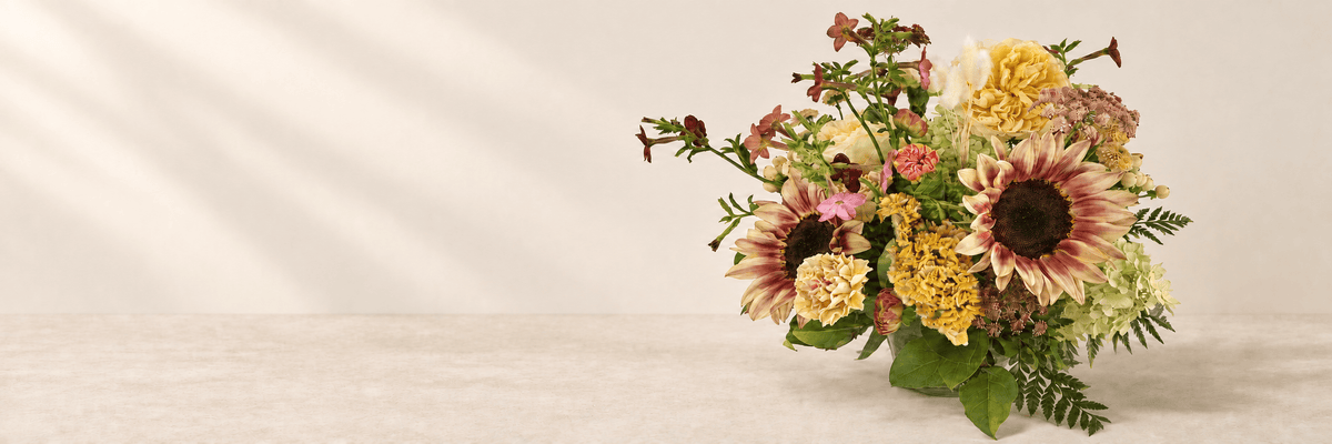 Autumn flowers with burgundy sunflowers and golden blooms on a warm oatmeal surface.